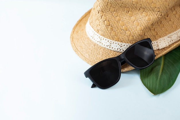 Straw hat and sun glasses on light blue wall