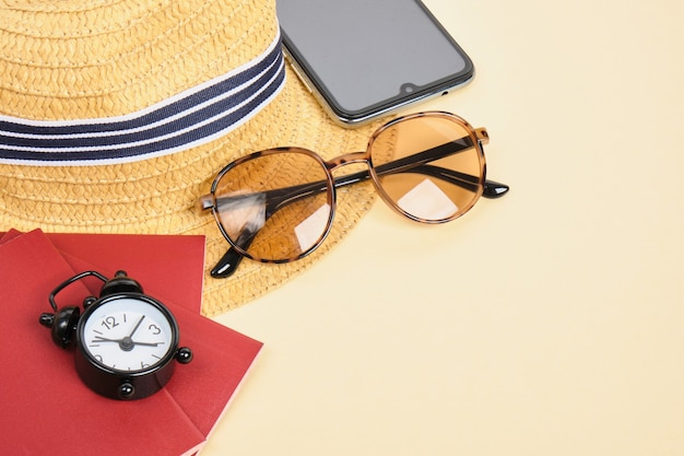 Straw hat, sunglasses, alarm clock and passport on beige background, time for travel and beach vacation concept