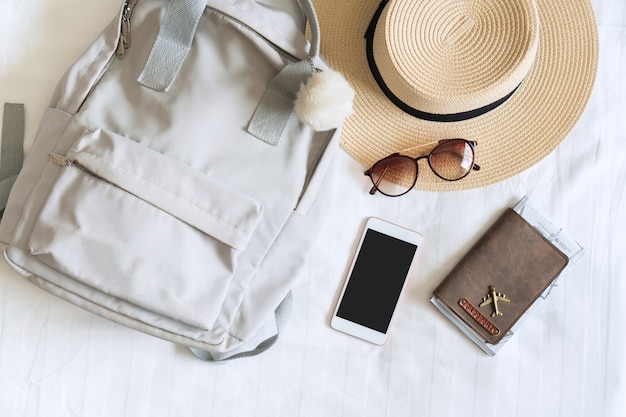Straw hat, sunglasses, bag, passport and smartphone of woman traveler on bed in modern hotel room. Travel, relaxation, journey, trip and vacation concepts. Top view  and copy space.