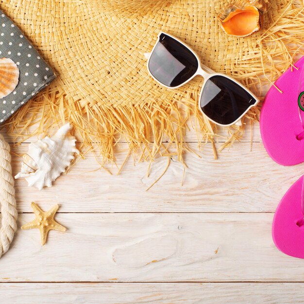 Straw hat sunglasses flip flops and beach bag on white wooden background