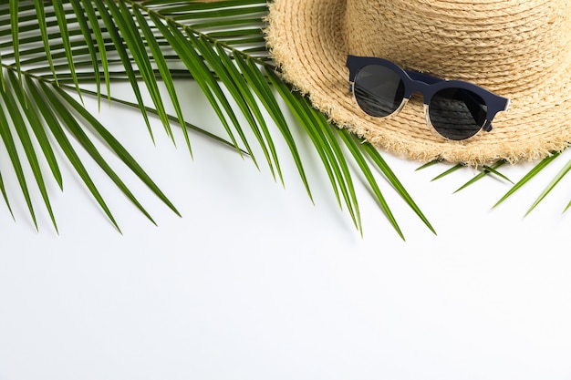 соломенная шляпа, солнцезащитные очки и пальмовые листья на белом фоне