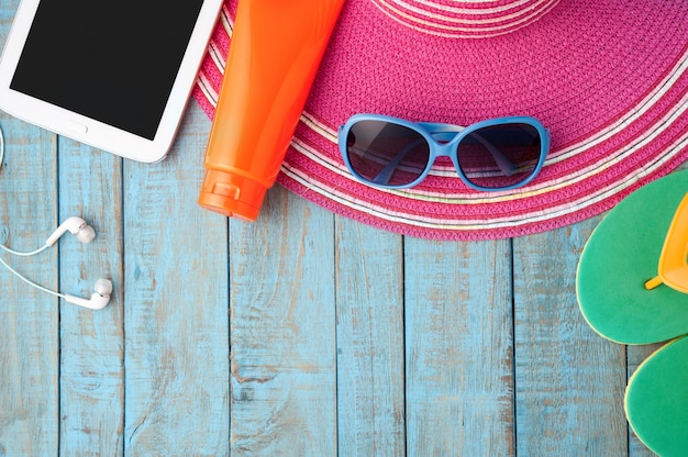 Straw hat tablet and sunglasses on blue wood.