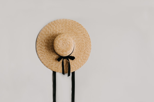 A straw hat with a black ribbon isolated on a grey wall.