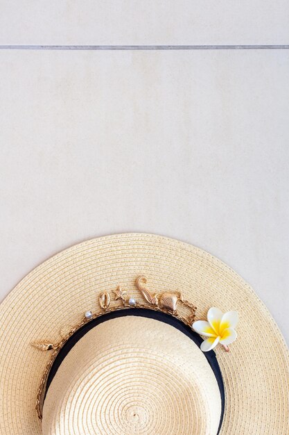 Straw hat with a necklace with shells and pearls and the plumeria flower on the tiled floor