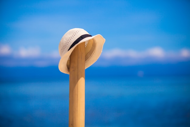 Straw hat at wooden fence on the white sandy beach with an ocean view