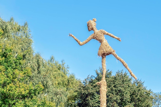 Straw sculpture of a girl in the park on the sky background