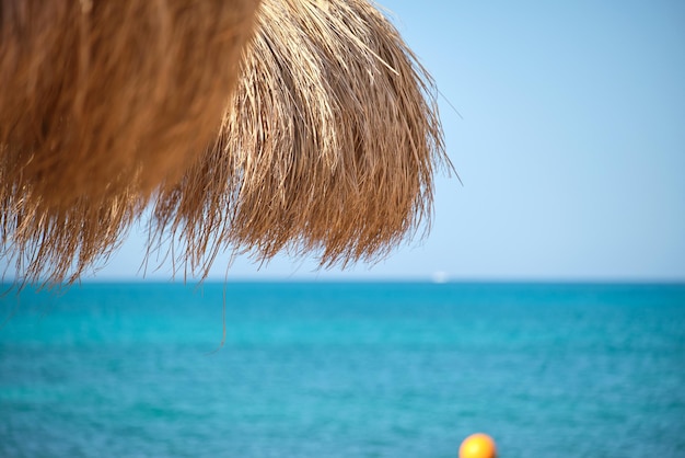 Straw shade umbrella in sea tropical region against blue vibrant sky in summer