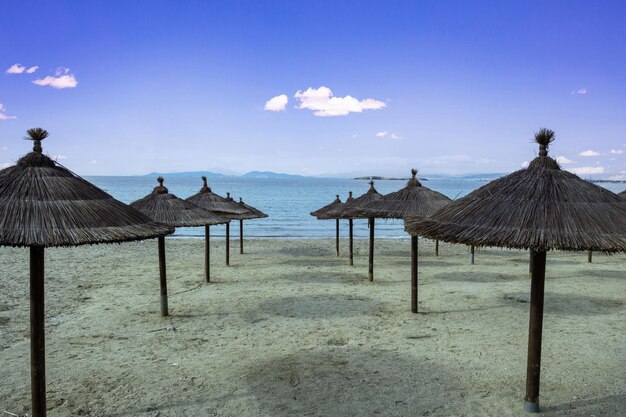 Straw umbrella in row on empty sandy beach Winter day sea sky background Holiday in Greece