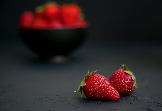 Strawberries on a black bowl and on black surface