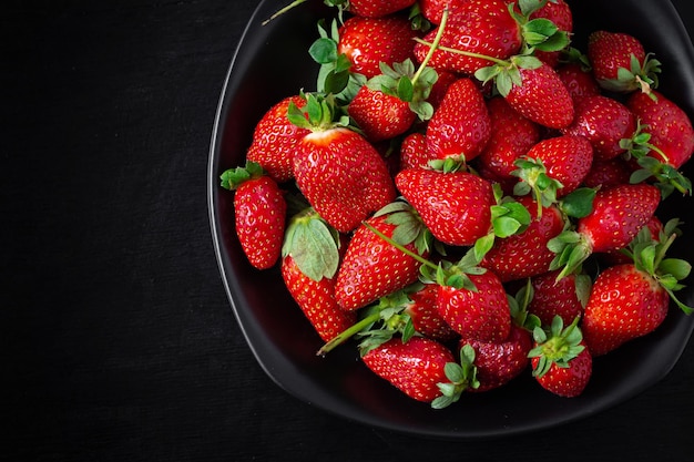 Fragole in un piatto nero su sfondo scuro vista dall'alto sopra