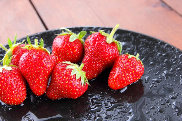 Strawberries on black plate red berries on wooden background copy space