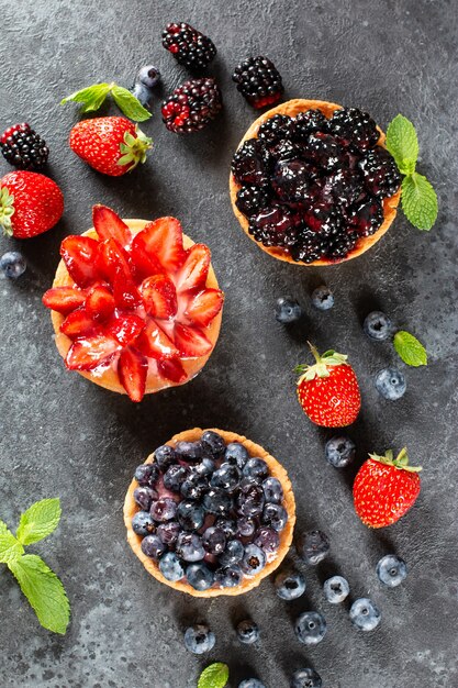 Strawberries, blueberries, blackberries tartlets with chocolate ganache, fresh berries and mint leaves, selective focus. Fresh fruit tart, freshly homemade fruit cake on a table