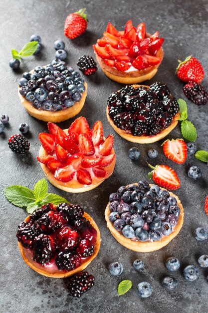 Strawberries, blueberries, blackberries tartlets with chocolate\
ganache, fresh berries and mint leaves, selective focus. fresh\
fruit tart, freshly homemade fruit cake on a table