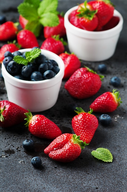 Strawberries and blueberries in bowls on a black table