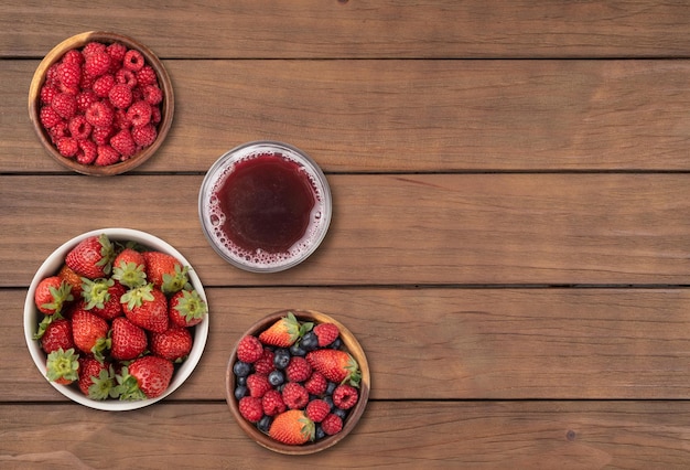 Strawberries blueberries and raspberries in bowls with juice over wooden table with copy space