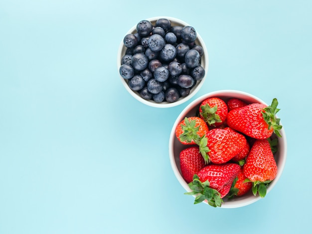 Strawberries and blueberries in white bowls on a blue bright background