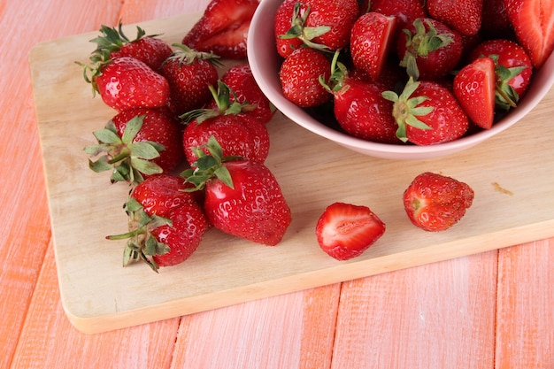 Strawberries in bowl on cutting board on wooden table