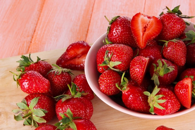 Strawberries in bowl on cutting board on wooden table