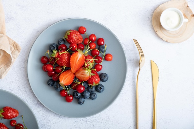 Strawberries cherries and blueberries on a plate with a knife and fork top view