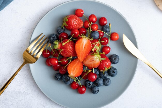 Strawberries cherries and blueberries on a plate with a knife and fork top view