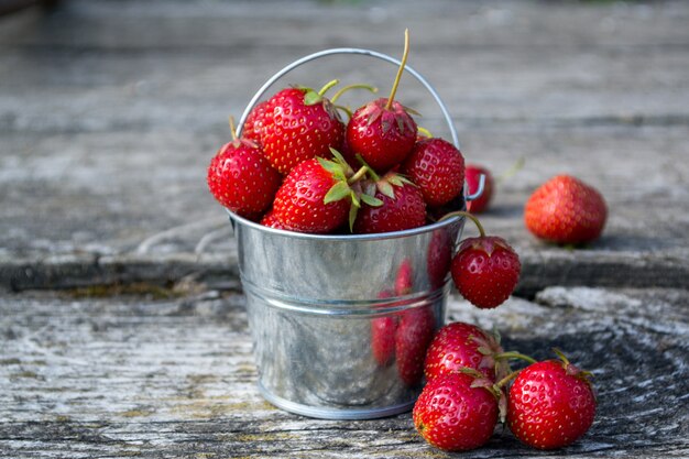 Strawberries in a decorative bucket on an old wooden surface.