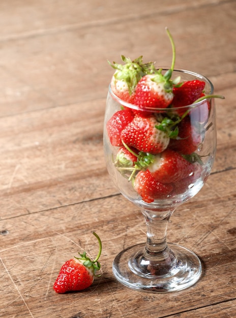 The strawberries in a glass on wood floor