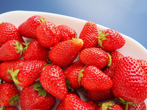 Strawberries on a plate blue background White dishes and ripe delicious red large strawberries