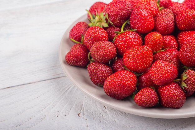 Strawberries on a plate on a white wooden background