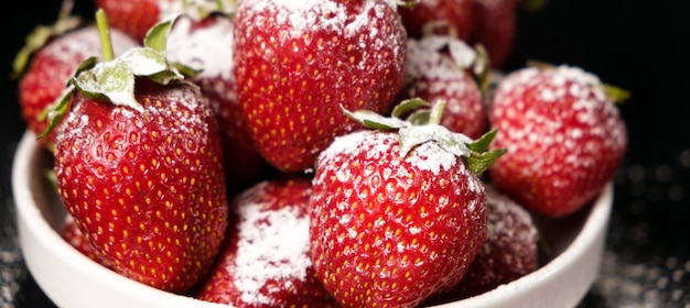 Strawberries in a plate with powdered sugar on a black background