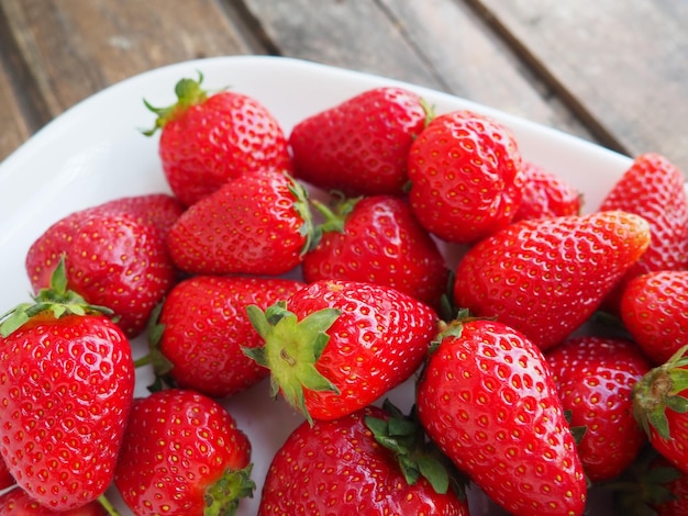 Strawberries on a plate wooden background White dishes and delicious red large garden strawberries Healthy food vitamins and a vegetarian diet Still life with food Copy space Flat lay