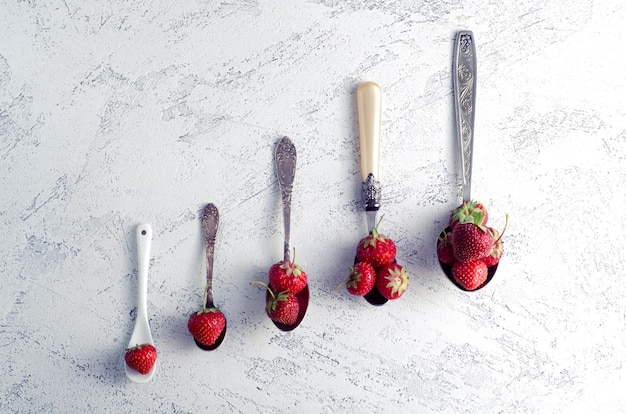 Foto fragole in cucchiai di diverse dimensioni. estate e concetto di mangiare sano