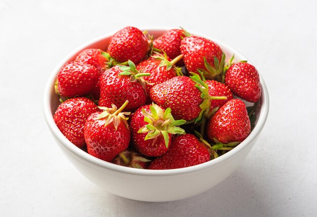 Strawberries in a white bowl closeup on a light background