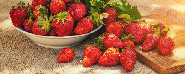 Strawberries on a white plate and a wooden cutting board on the table Horizontal banner