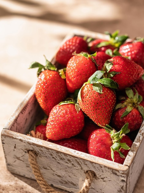 Strawberries in white rustic box on brown textured background with window shadows close up