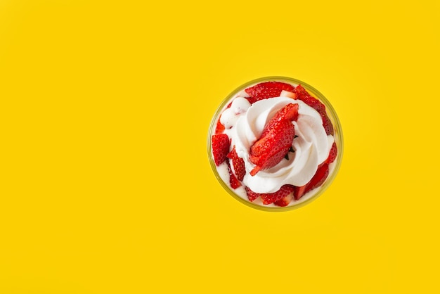 Photo strawberries with cream in a glass cup on yellow background top view copy space