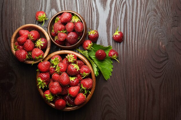 Strawberries with green leaves in wooden bowls on brown table top view