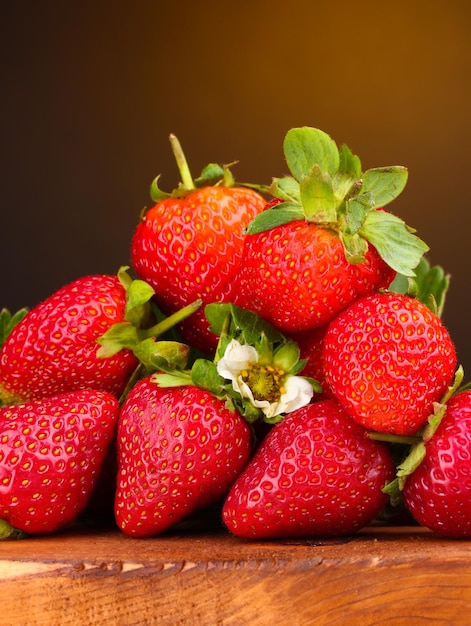 Strawberries with leaves on wooden table on brown background