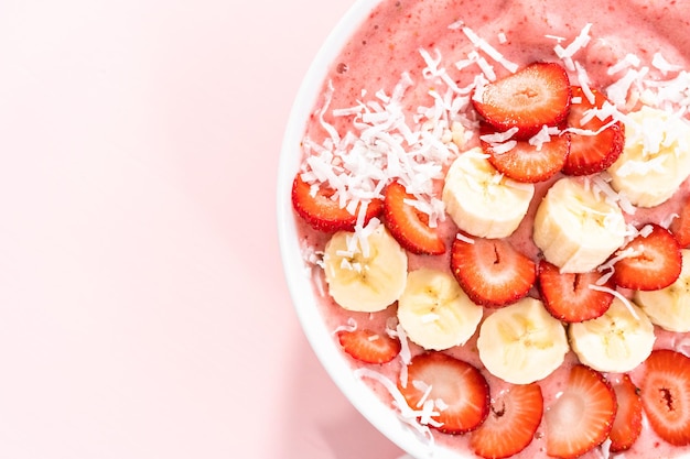 Strawberry and banana smoothie bowl garnished with coconut flakes and fresh fruits.