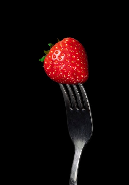 Strawberry berry closeup on a fork on a black background