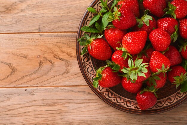 Strawberry berry Fresh red strawberry in ceramic rustic plate in basket on light wooden rustic table closeup Delicious juicy red berries Top view with copy space