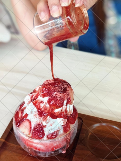나무 트레이에 있는 유리 컵에 있는 딸기 빙수.