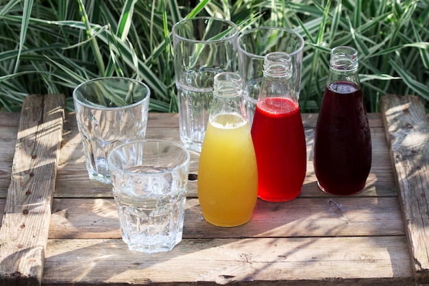 Strawberry, cherry and rhubarb syrups and glasses with water on a wooden table in the garden.