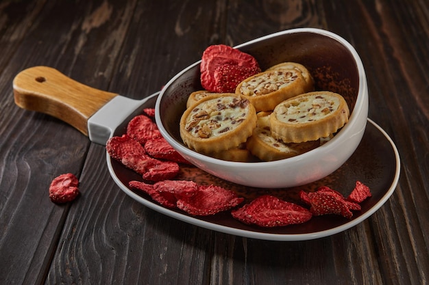 Strawberry chips and cookies with chocolate and cream are stacked in ceramic plate with wooden handle on dark wooden background 1Hundredpercent natural freezedried strawberries