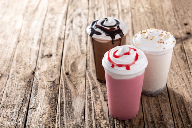 Strawberry, chocolate, and white iced milkshakes on wooden table