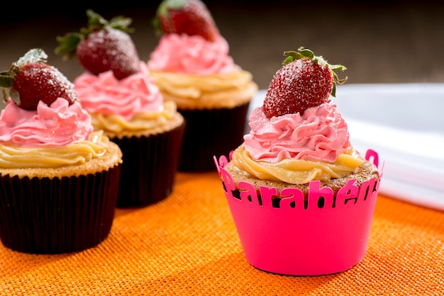 Strawberry cupcake with whipped cream in pink cupcake written happy birthday in portuguese