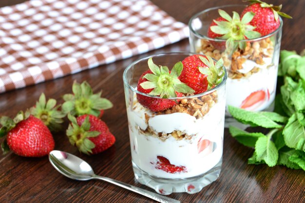 strawberry dessert with yogurt, muesli and mint leaves on the wooden background with a teaspoon