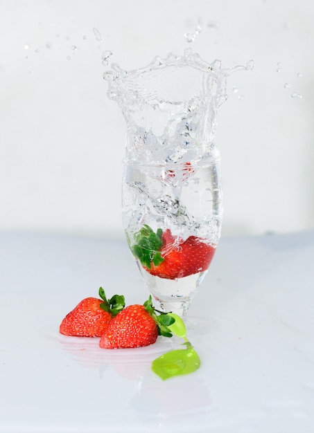 Photo strawberry fruit drops onto a wine glass freeze motion of the water splash white background