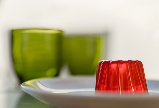 Strawberry gelatin on a white plate and two green glasses on the background