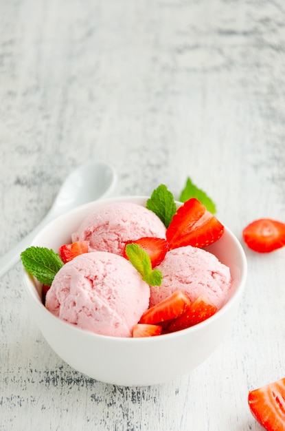 Gelato alla fragola in una ciotola con fragole fresche e menta su uno sfondo di legno. copia spazio.