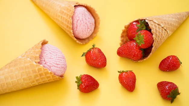 Strawberry ice cream in a waffle cone ice cream and berries on a yellow